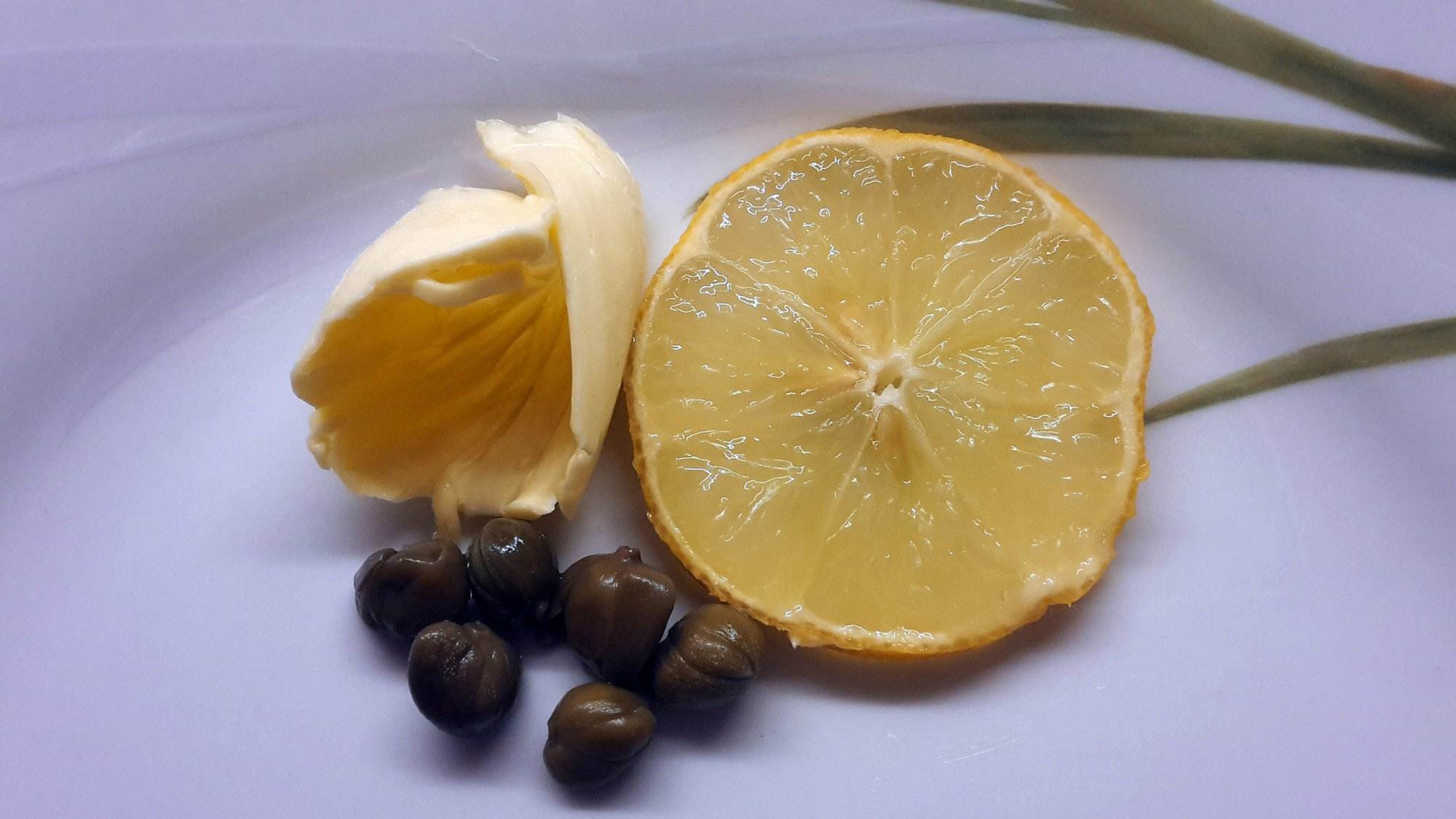 Eine Zitronenscheibe und schwarze Oliven auf einem weißen Teller.