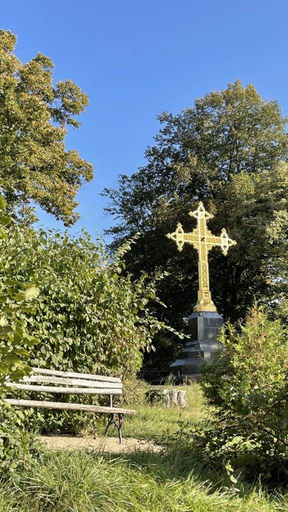 Ein goldenes Kreuz sitzt auf einer Bank in einem Park.