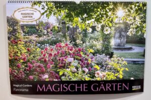 Naturkalender 2025, Cover eines Kalenders mit dem Titel „Magische Gärten“ mit einem Garten mit blühenden rosa und weißen Blumen, Grünpflanzen und einem Steinbrunnen.