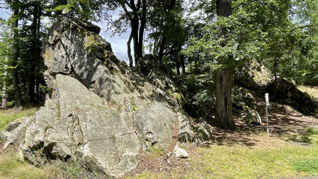 Große, zerklüftete Felsformationen, umgeben von Bäumen in einem Waldgebiet an einem sonnigen Tag.