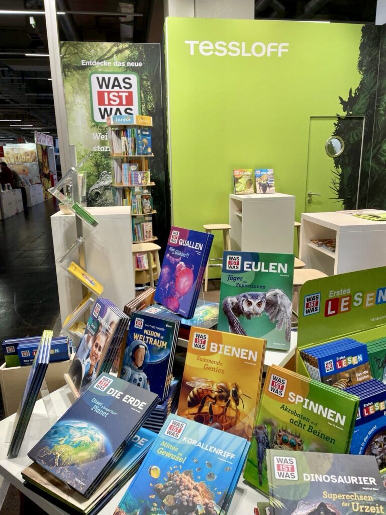 Ausstellung von Kinderbüchern zu Wissenschaft und Natur, einschließlich Themen wie Bienen, Dinosaurier und Weltraum, an einem Tessloff-Stand.