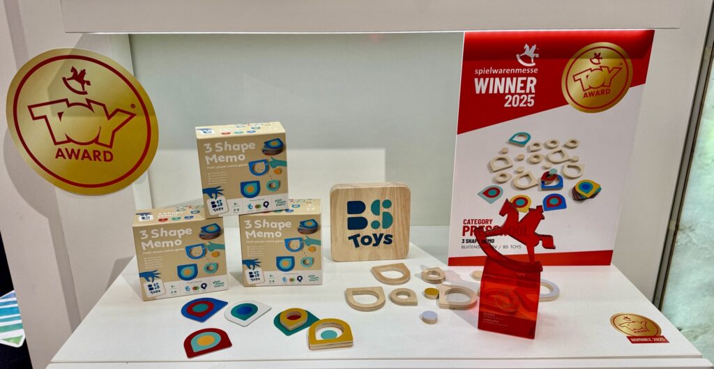 Ausstellung von BS Toys-Produkten, darunter Holzformkästen. Auszeichnungen und Anerkennungen sind sichtbar, darunter ein Toy Award und der Spielwarenmesse-Gewinner 2025.