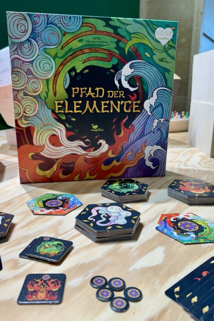 Brettspiel „Pfad der Elemente“ auf einem Tisch mit bunten Spielsteinen und Karten, versehen mit Elementsymbolen und Motiven.