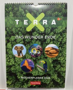 Umschlag eines Wochenplaners 2026 mit dem Titel "Terra: Das Wunder Erde" mit Abbildungen eines Elefanten, tropischen Fisches, einer Wüste, eines Vulkans und eines Tukans auf einem Hintergrund aus grünen Bäumen.