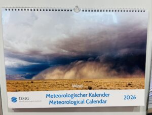 Ein Wandkalender mit dem Titel "Meteorologischer Kalender 2026" mit einem Titelbild, das einen dramatischen, bewölkten Himmel über einer trockenen Wiese zeigt.