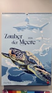 Das Cover des Wandkalenders 2026 trägt den Titel "Zauber der Meere" und zeigt im Vordergrund eine Meeresschildkröte und darüber zwei schwimmende Haie.
